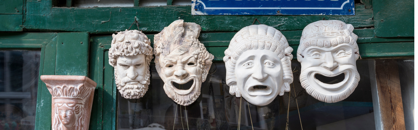 Four ancient theatre masks are hanging on a wall. They display emotions of excitement and fear. The masks are made out of clay.